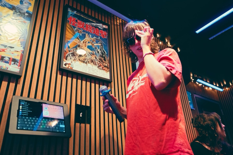 A singer holding a microphone beside the room’s song-selection tablet