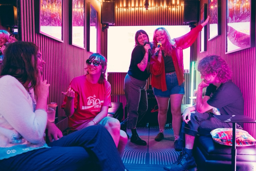 A group singing into microphones while friends cheer them on